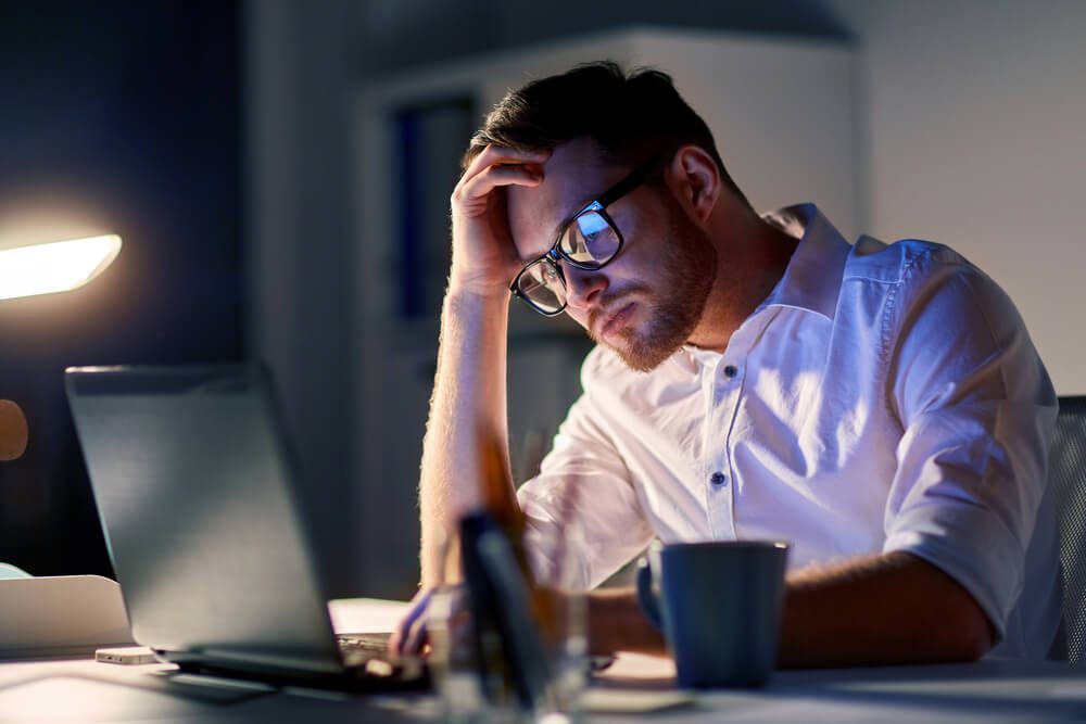business, overwork, people, deadline and technology concept - stressed businessman in glasses with laptop computer thinking at night office