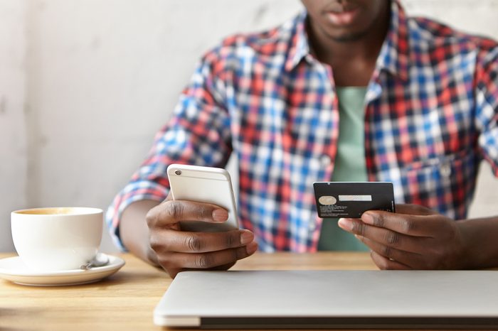 Close up shot of male hands holos mug debit cad and mobile phone, entering data for web-site form, going to pay for online order. People, lifestyle, modern technologies and e-commerce concept