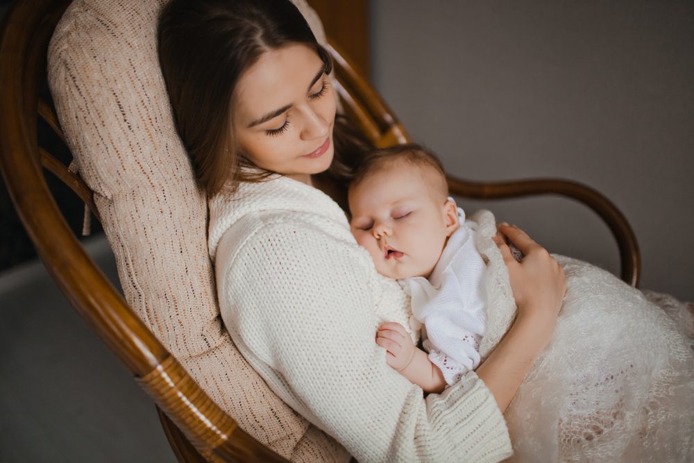 young mother holding her newborn baby sitting in armchair