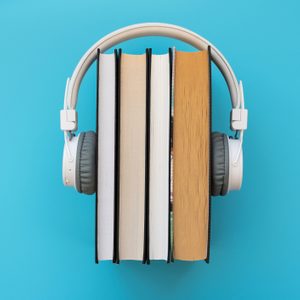 Headphones rest on upright books, forming a symmetrical arrangement against a solid blue background.