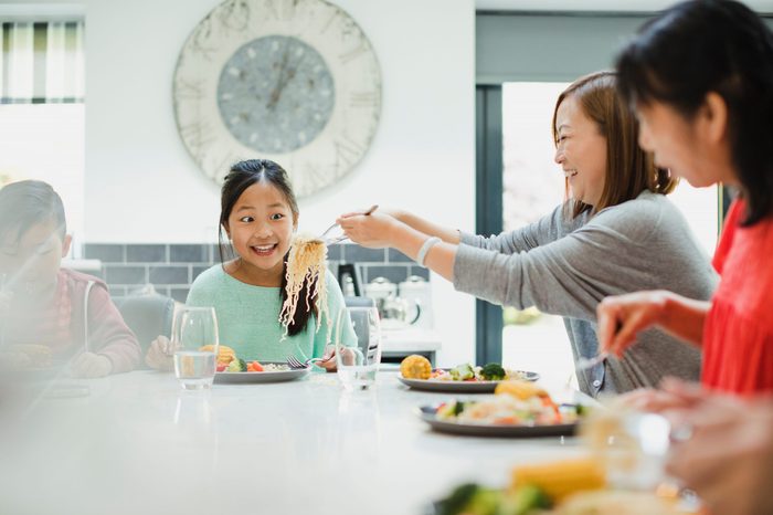 Little girl is looking excited as her mother puts another serving of noodles on her plate at a family dinner at home.