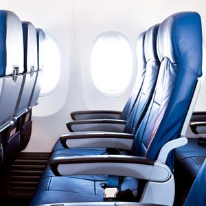Airplane seats aligned, facing forward, inside a plane cabin with visible windows on the left.