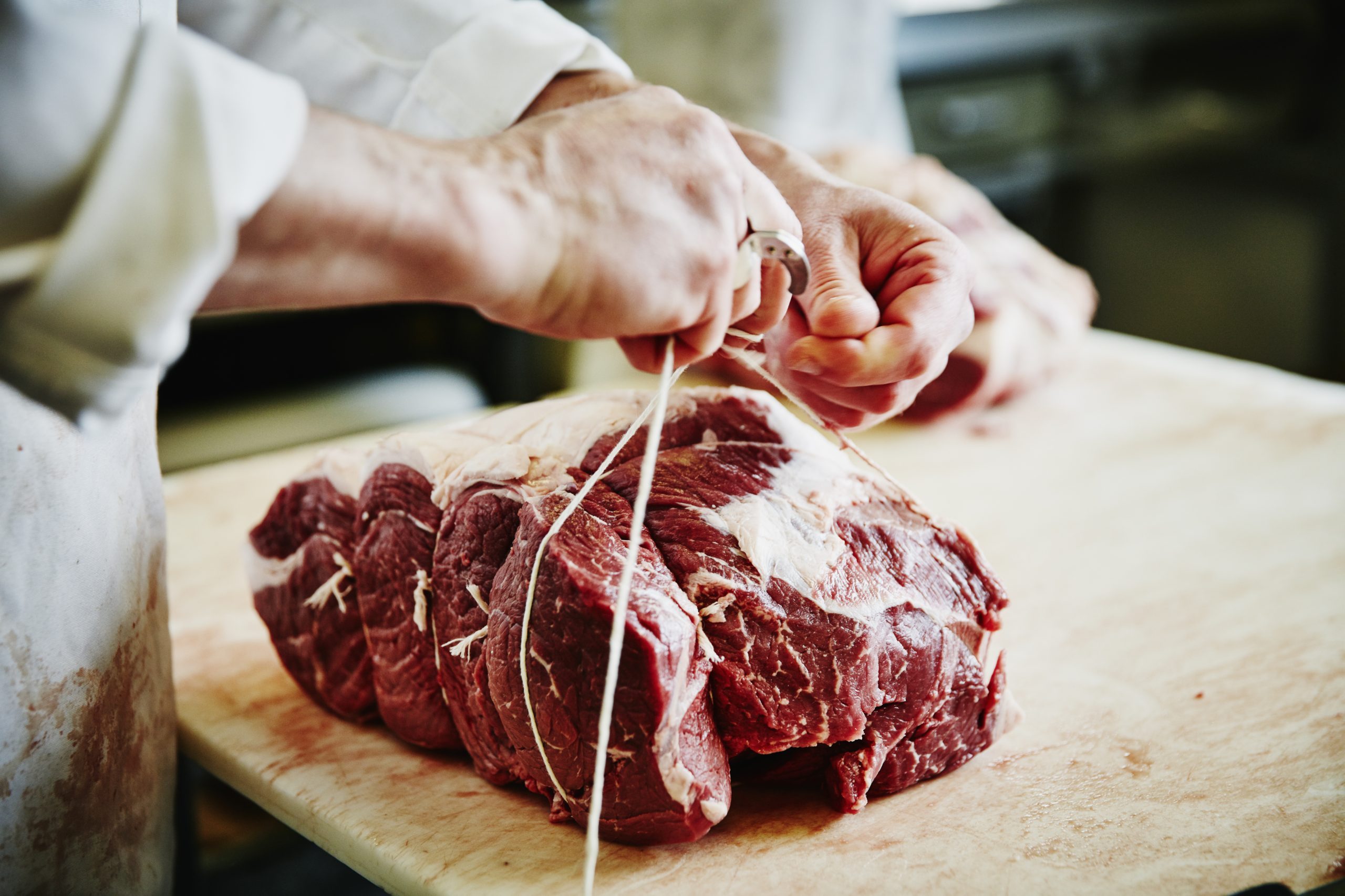 Butcher tying up beef bottom round at counter