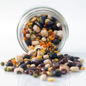 A glass jar spills colorful mixed legumes onto a white surface, creating a vibrant spread of beans and lentils.