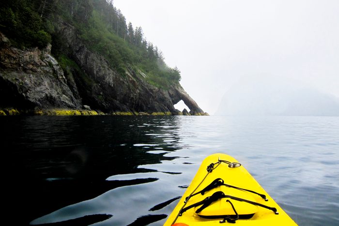 A pair of sea kayakers paddles during a grey Alaska summer day on the Pacific Ocean along Fox Island, Alaska.