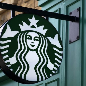 Circular logo featuring a mermaid, hanging prominently outside, with a green and white color scheme on a building facade.