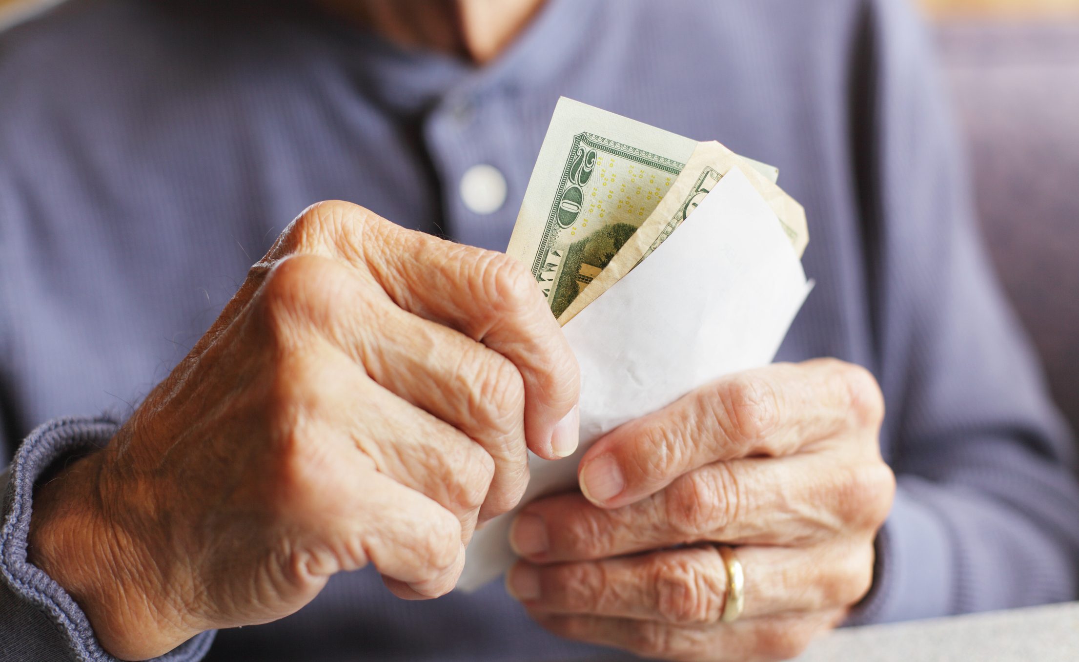 Hands hold dollar bills in a white envelope, set against a blue shirt background.