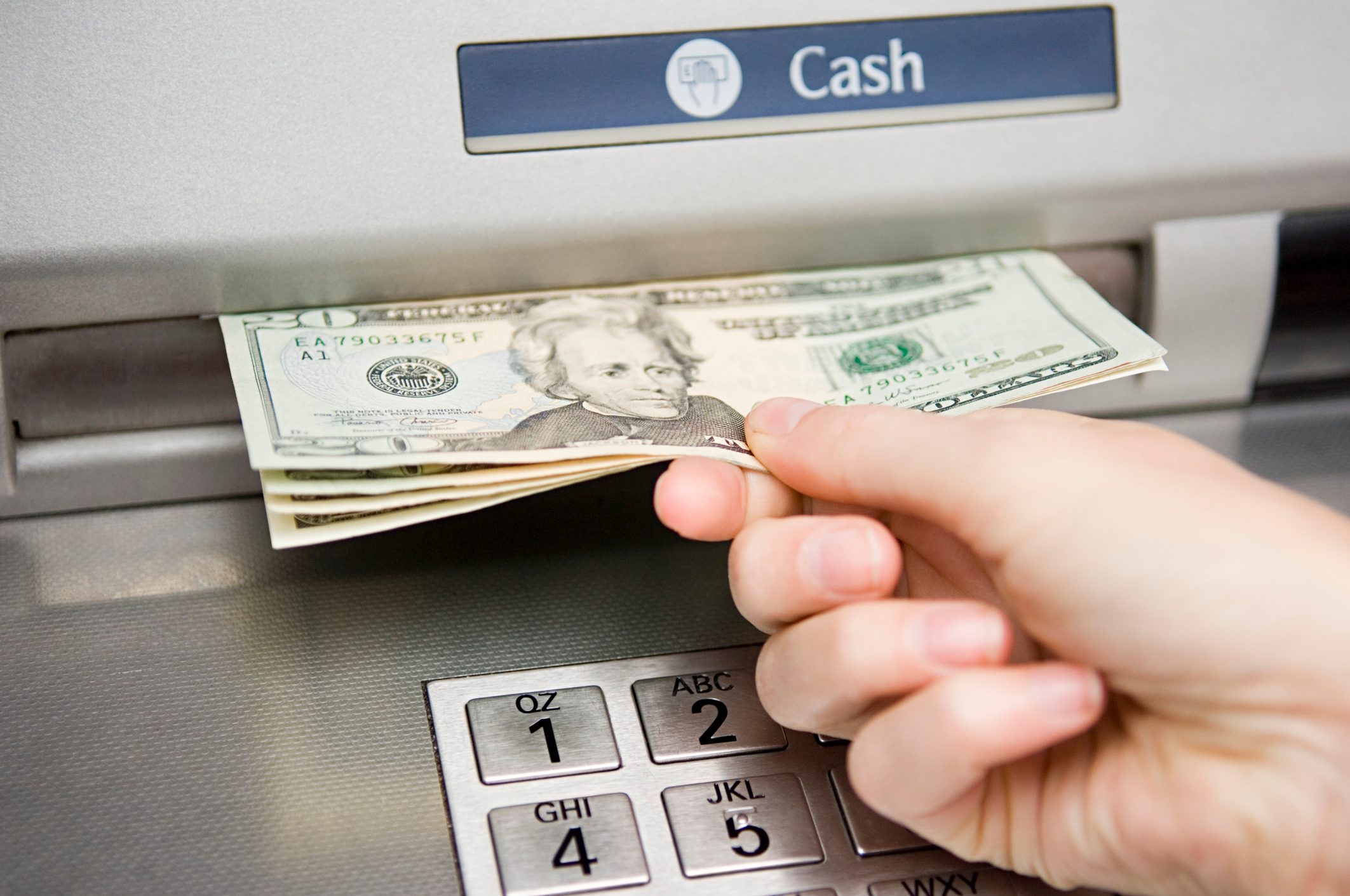 Hand withdrawing cash from an ATM, above a keypad.