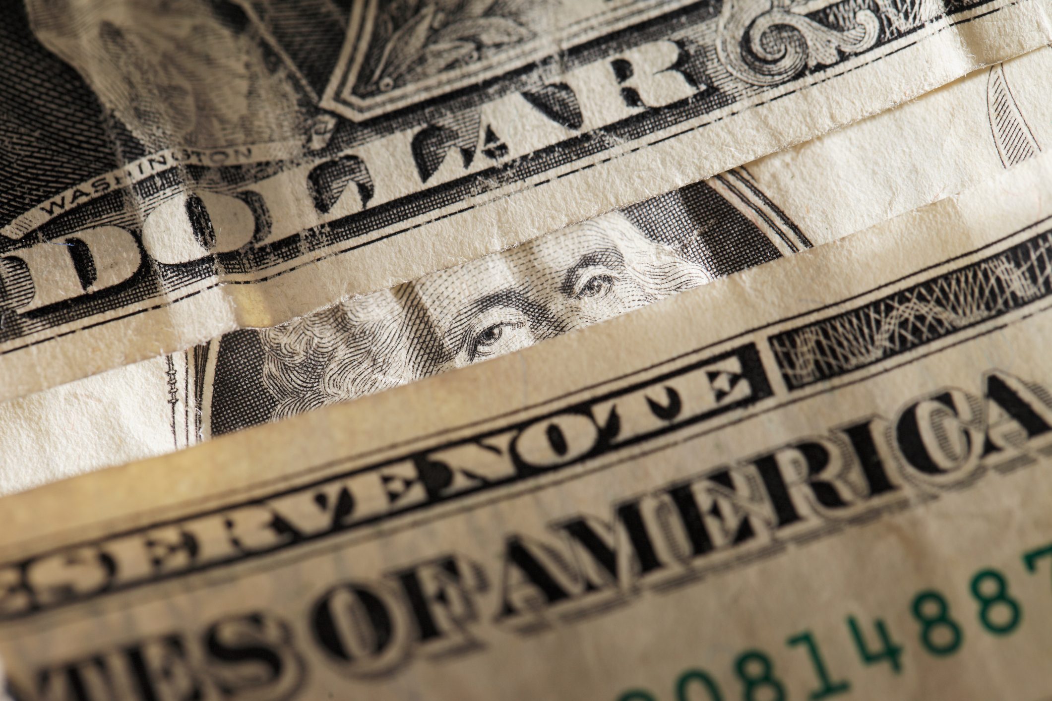 Dollar bills layered closely, showing partial text and a person's eyes, in a detailed close-up view.