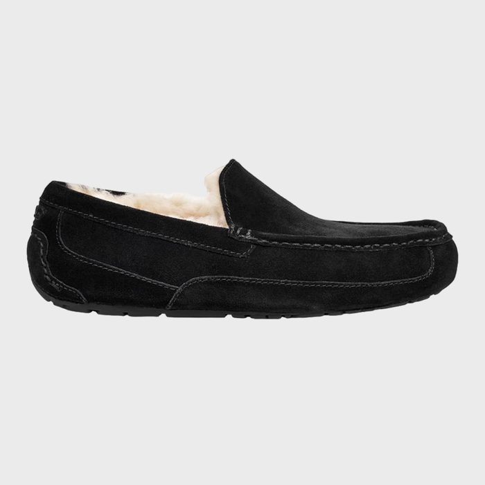 A black suede slipper with white fuzzy lining sits against a plain background.