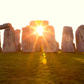 Stonehenge standing; sunlight shines through stones; grassy field surrounds.