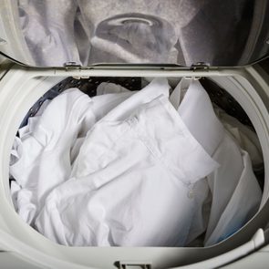 Laundry sits in an open washing machine, with white shirts visible inside, ready to be washed.