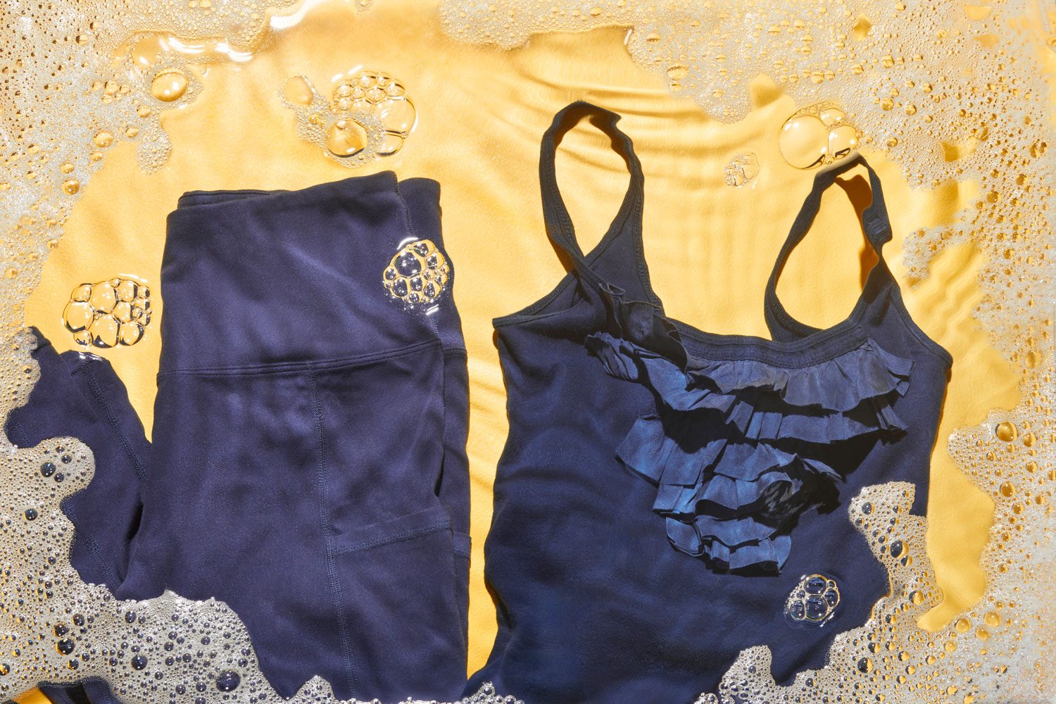 Athletic tights and delicate tank top on yellow background with soap bubbles around