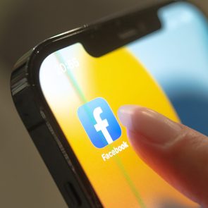 Finger tapping Facebook app icon on a smartphone screen, displaying time as 20:55, against a blurred, colorful background.