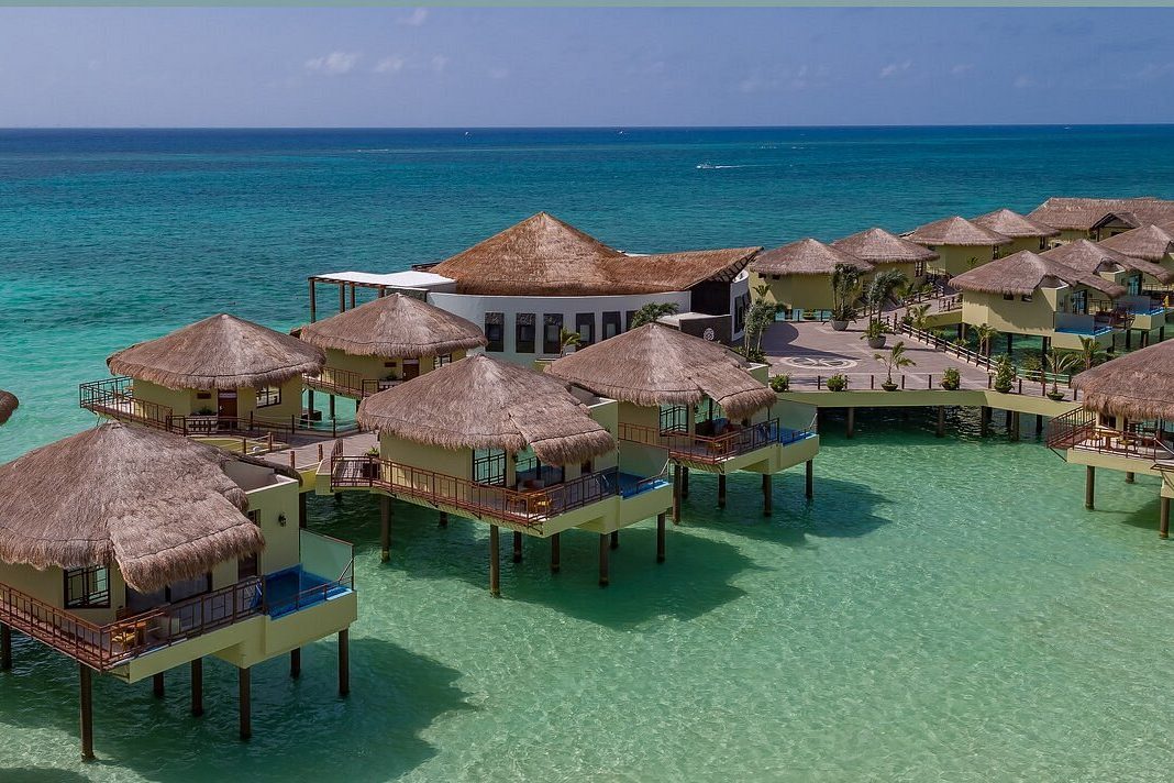 Overwater bungalows sit on stilts, surrounded by turquoise sea, under clear blue sky.