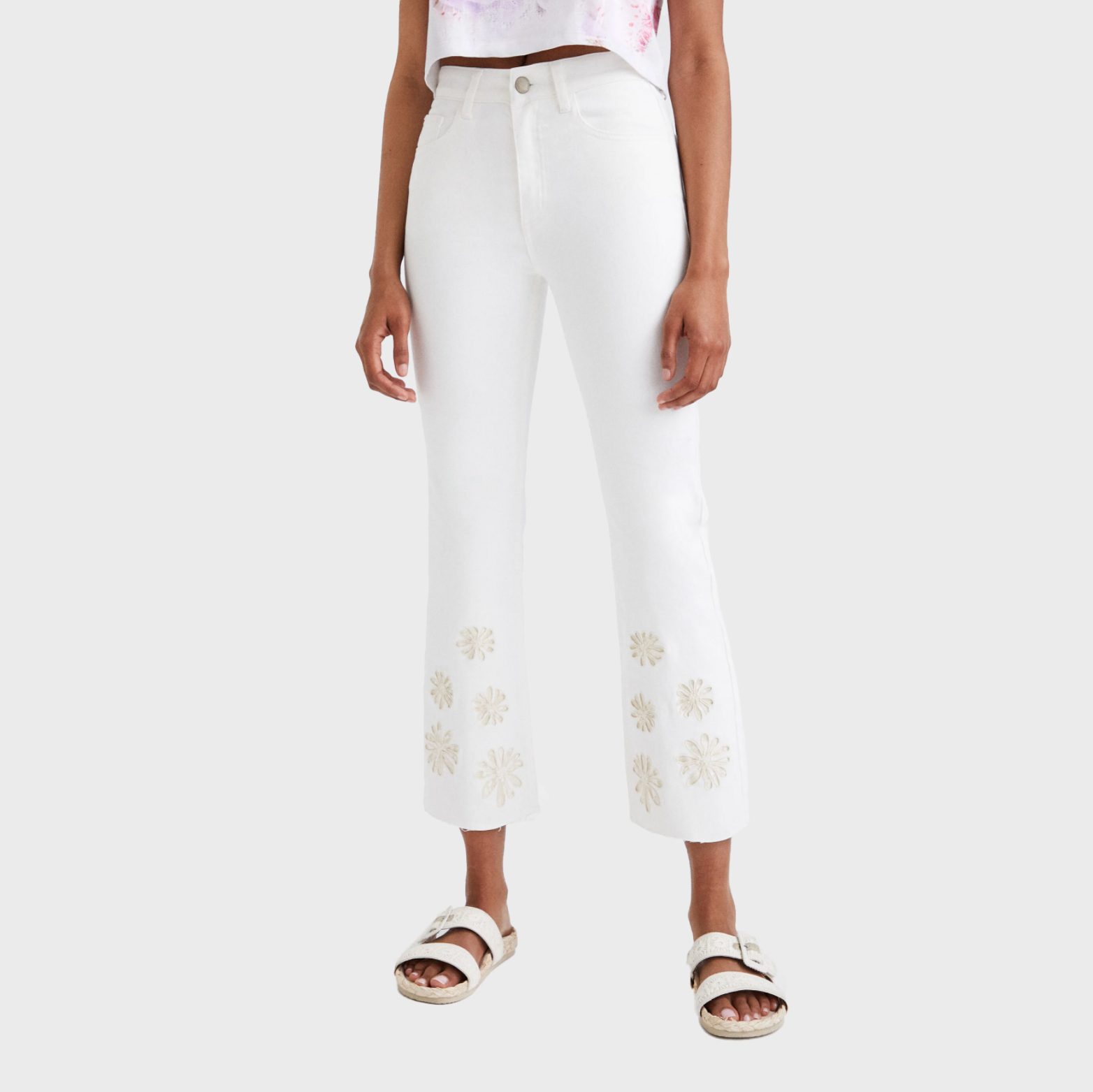 White embroidered pants hang loosely on a person, paired with sandals and a cropped top, against a plain background.