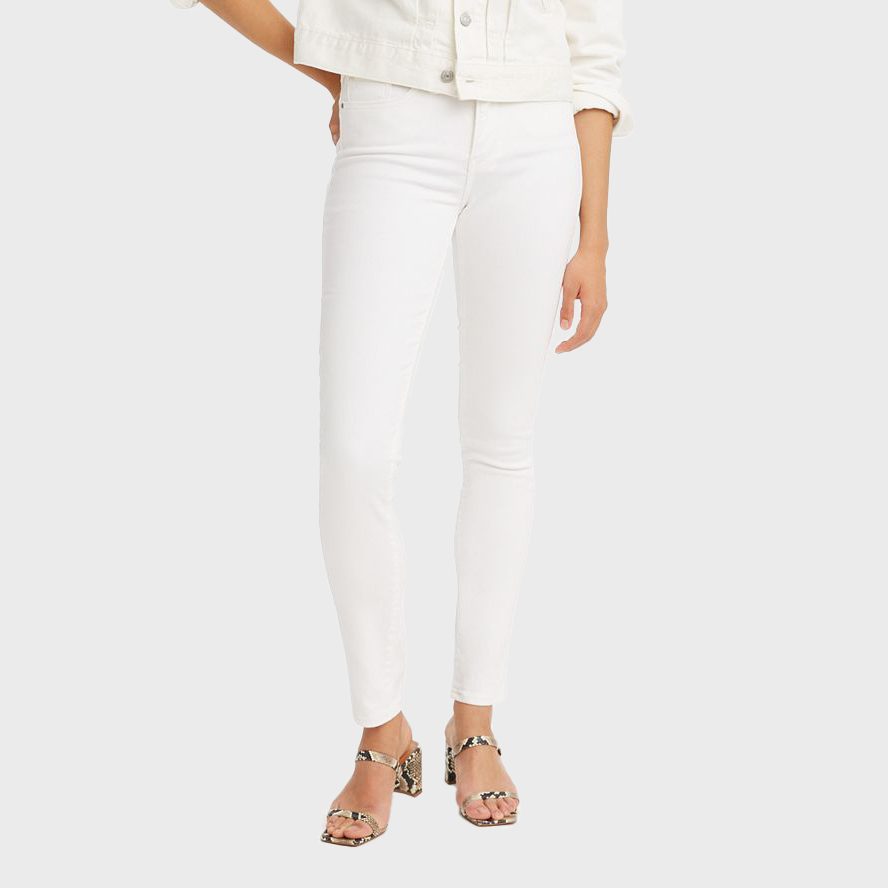 A person models white skinny jeans and a matching jacket, standing on a plain background wearing snakeskin-patterned sandals.