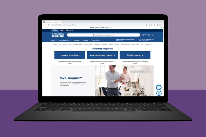 A laptop displays a Bed Bath & Beyond wedding registry webpage showing options to create, manage, or find a registry amidst a kitchen-themed background.