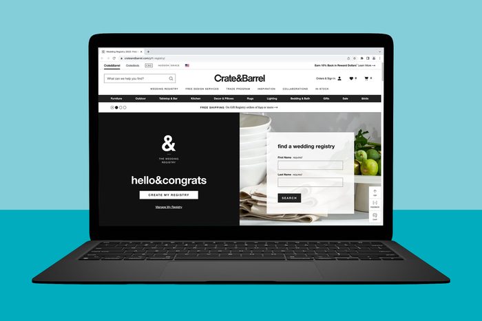 Laptop displays a Crate & Barrel wedding registry webpage, prompting users to create or search registries; background shows plates and green apples.