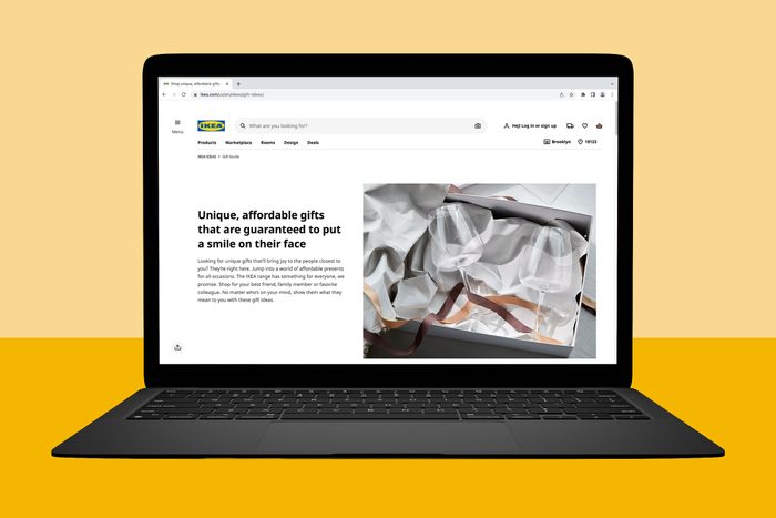 Laptop displaying a webpage featuring gift ideas; includes product categories, search bar, and promotional text about affordable gifts beside an image of wine glasses.