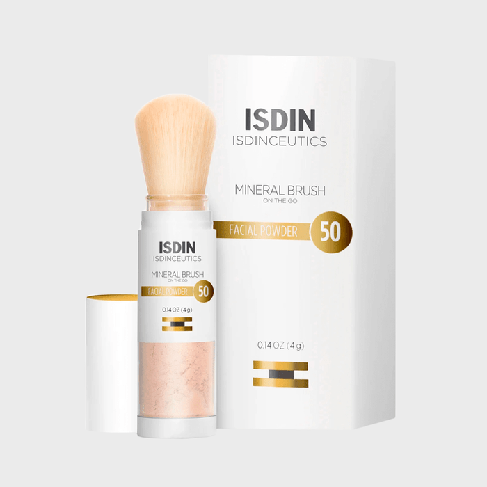 Brush dispenses powder beside branded packaging on a light background; text reads 