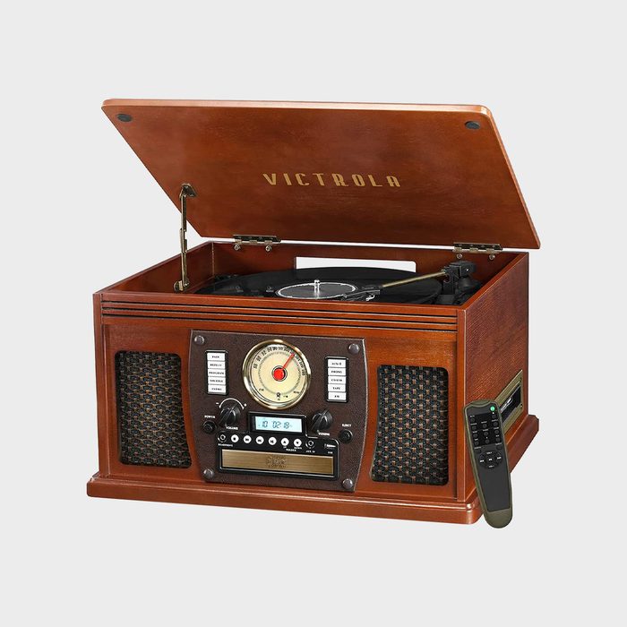 A wooden vintage-style turntable plays a record, surrounded by control buttons, speakers, and a remote. 