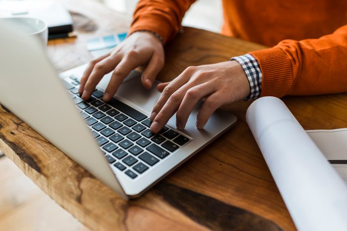 Close-up of man using laptop next to construction plan at desk