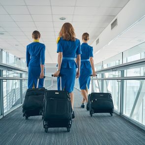 Flight attendants pull suitcases while walking through a bright, modern airport corridor.