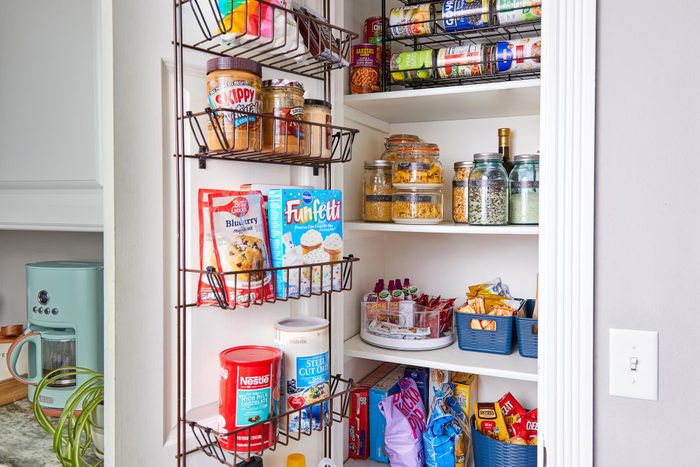 Shelves hold neatly organized pantry items, including jars, snacks, and baking mixes. A coffee maker sits on a nearby counter.