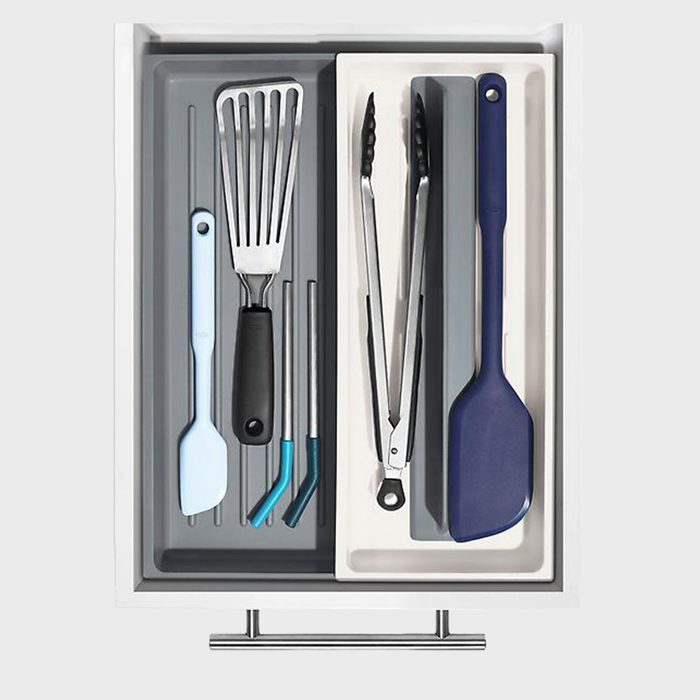Utensils organized in a drawer; spatula, tongs, and straws, neatly arranged in compartments, surrounded by a white and gray interior.