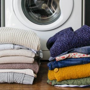 Two stacks of folded sweaters rest on a wooden floor in front of a white washing machine.