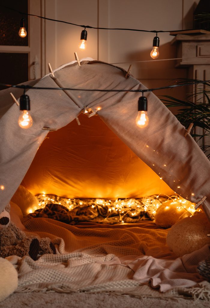 handmade tent with blankets, pillows, toys and lights in room