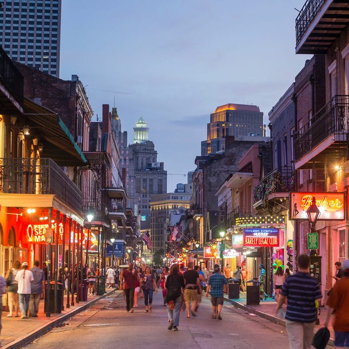 People walk under colorful neon signs along a bustling city street at dusk, surrounded by historic buildings and vivid lights.
