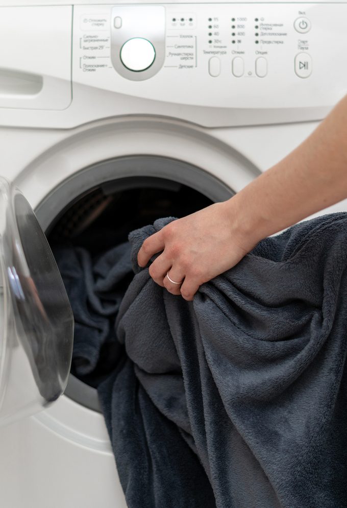 Cropped photo of woman hands put laundry into the white washing machine. She standing inside bright apartment with light interior