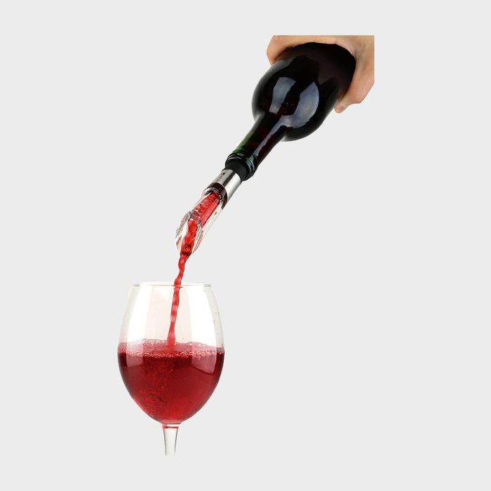 A wine bottle pours red wine into a glass, set against a plain background.