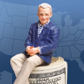 A doll sits atop a roll of U.S. dollar bills against a blue background with a map outline.