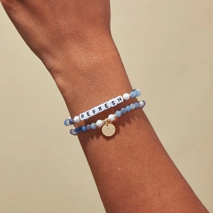 A hand wears bracelets; one with blue beads and 