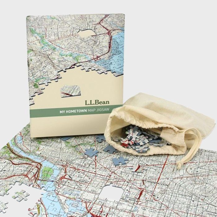 Puzzle pieces spill from a cloth bag; an L.L.Bean map jigsaw box rests beside a partially completed puzzle on a table.