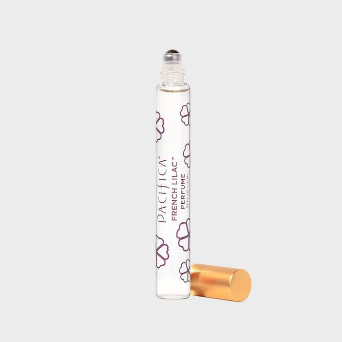 A clear perfume roller bottle stands, decorated with floral designs, lid off beside it, on a plain white background. Text: 