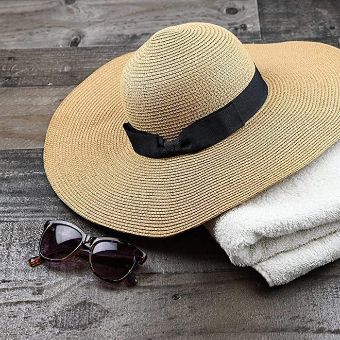 A straw sun hat rests on folded towels next to sunglasses on a wooden surface.