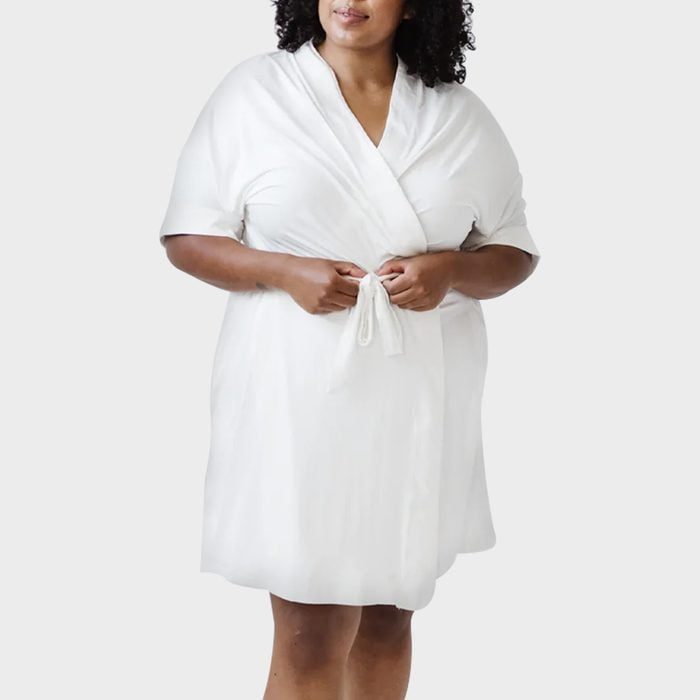 A person wears a white robe, holding the belt, against a plain background.