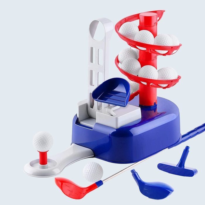 Golf ball dispenser releases balls onto a tee, featuring red and blue components. Miniature golf clubs are scattered nearby. Suitable for indoor practice.