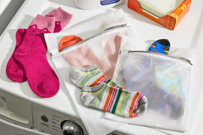 Socks with matching pairs shown in and around mesh laundry bags arranged on top of a washing machine