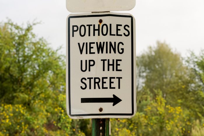 A metal road sign directs viewing up the street, indicating pothole presence.