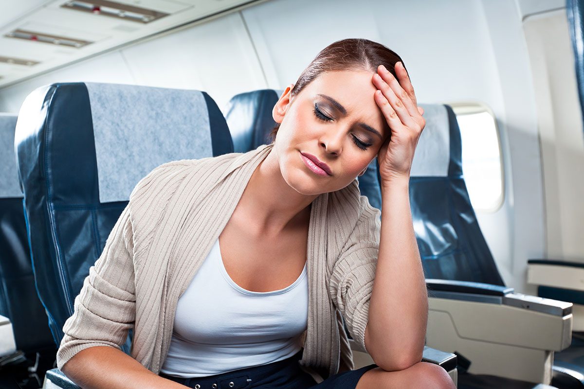 A young woman sitting on an airplane and suffering from headache.