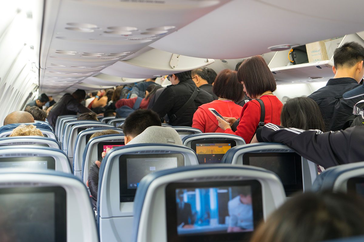 People are standing and sitting in an airplane cabin before disembarking