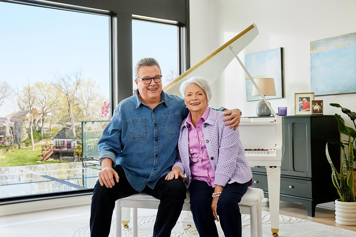 Eric Stonestreet and mother Jamey Stonestreet sit close to each other on a piano bench in front of a white grand piano in a sunlit room